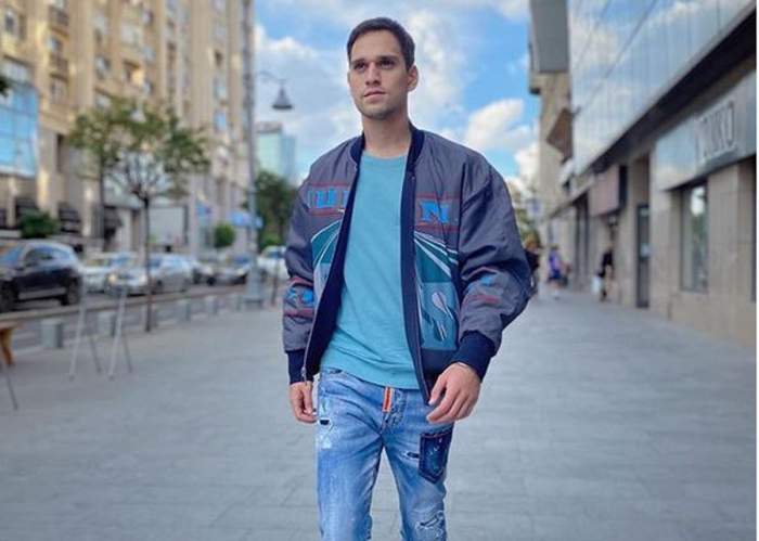 Vlad Gherman merge pe stradă. Artistul poartă o geacă bleu și niște blugi