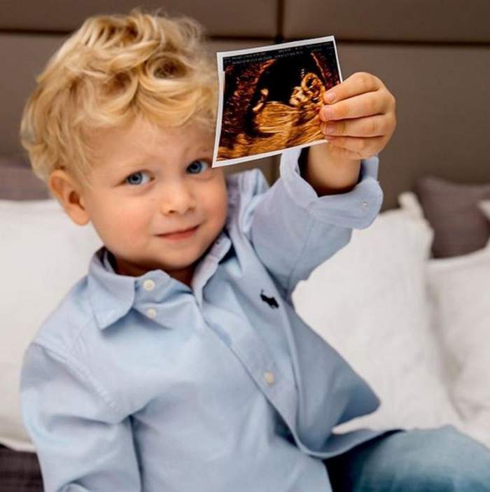Fiul Chiarei Ferragni ține în mână ecografia bebelușului mamei lui. Leo e îmbrăcat în cămașă bleu și blugi.