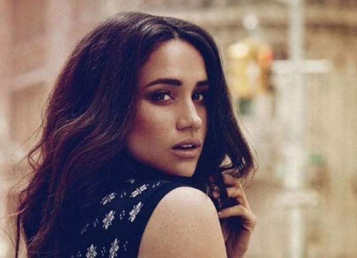 Meghan Markle poarta o rochie neagra fara maneci si are parul ondulat, desprins