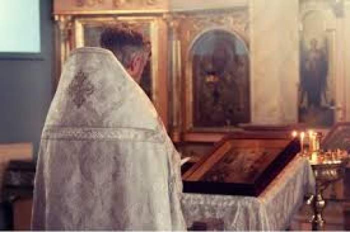 Fotografie cu un preot care se roagă în biserică