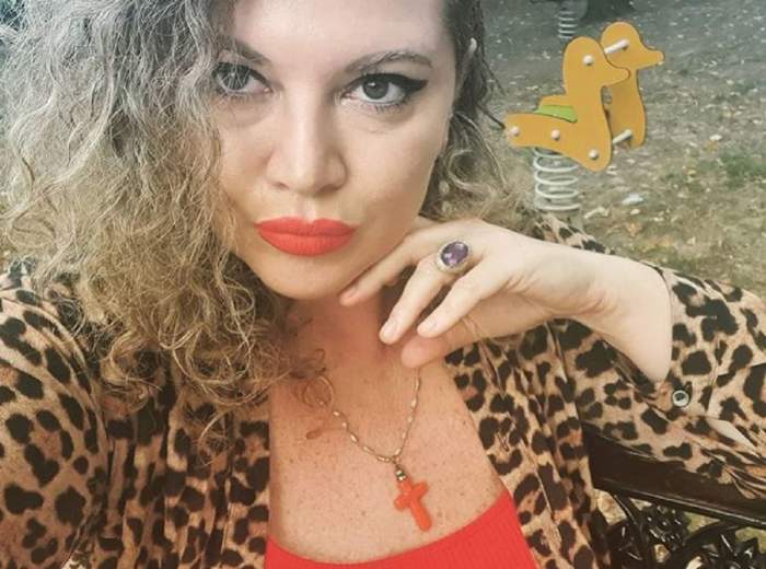 Oana Lis se află în parc. Vedeta poartă o bluză cu animal print și e dată cu ruj roșu.