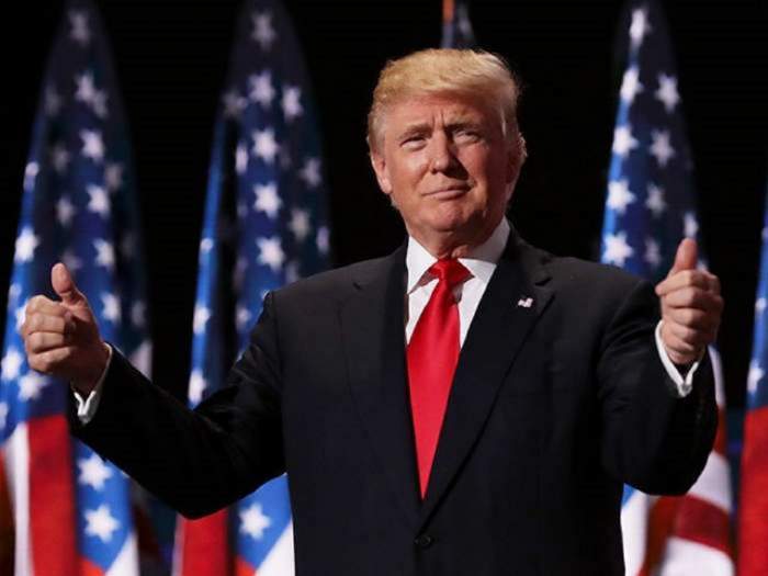 Donald Trump este in timpul unei conferinte oficiale, poarta costum si cravata rosie