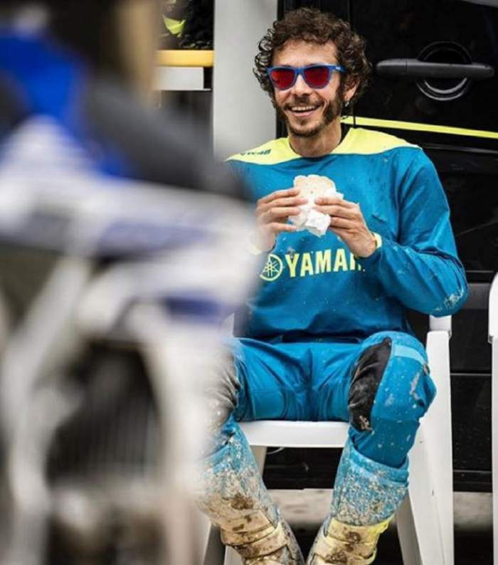 Valentino Rossi mananca un sendvis, sta pe scaun si poarta ochelari de soare