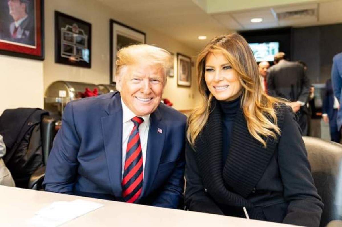 Donald și Melania Trump stau la masă. Președintele poartă un costum albastru, iar ea o ținută neagră.