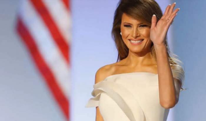 Melania Trump este la un eveniment public, face cu mana oamenilor si zambeste larg, poarta o rochie alba
