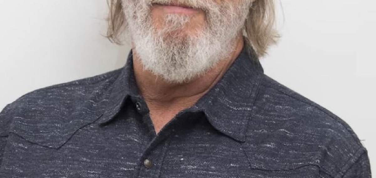 Jeff Bridges poartă un tricou gri. Actorul zâmbește.