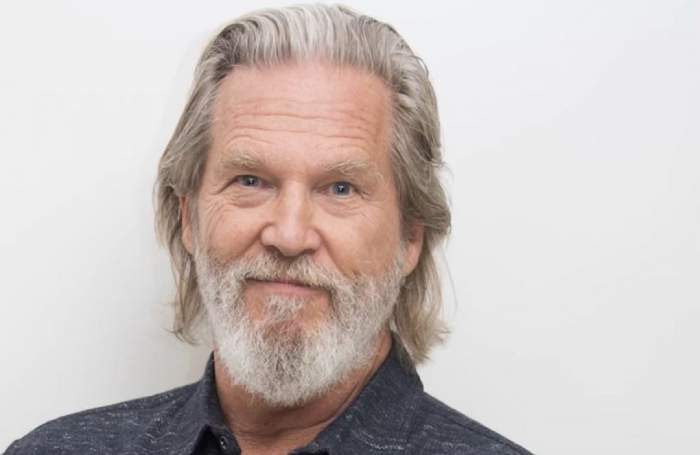 Jeff Bridges este îmbrăcat într-un tricou gri. Actorul zâmbește.