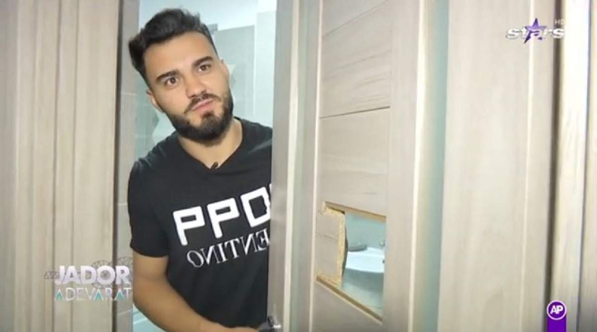 Jador poartă un tricou negru. Artistul se află în baie, lângă ușă.