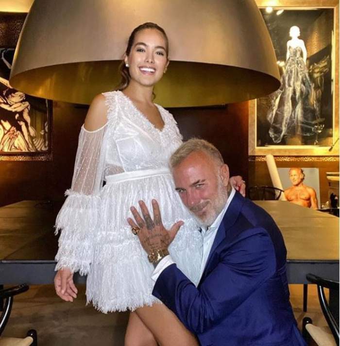 Gianluca Vacchi ii tine mana pe burtica iubitei sale, ea sta in picioare si poarta o rochie alba