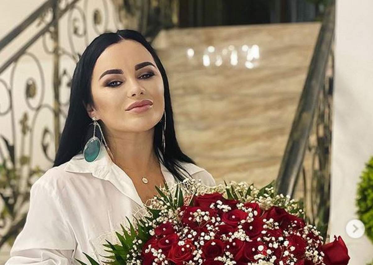 Carmen de la Sălciua poartă o cămașă albă. Artista ține în mână un buchet de flori albe și roșii.