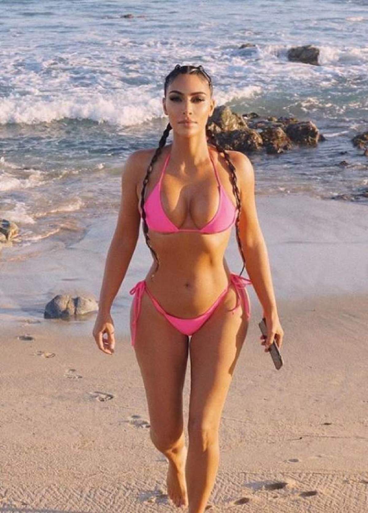 Kim Kardashian este la plaja, are un costum de baie roz si doua cozi impletite
