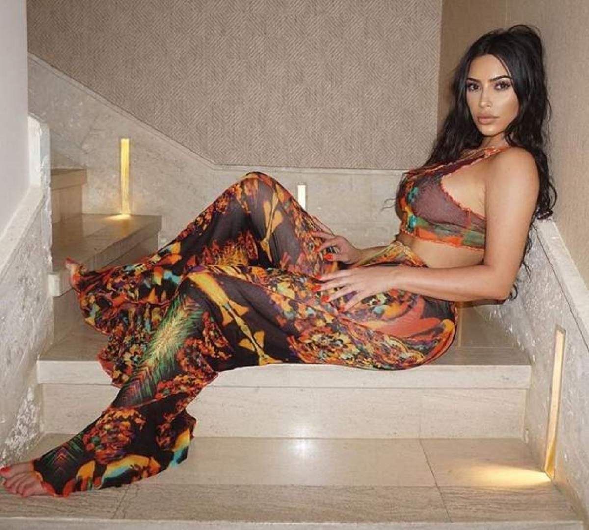 Kim Kardashian sta pe scari, poarta un set format din pantaloni cu model si top
