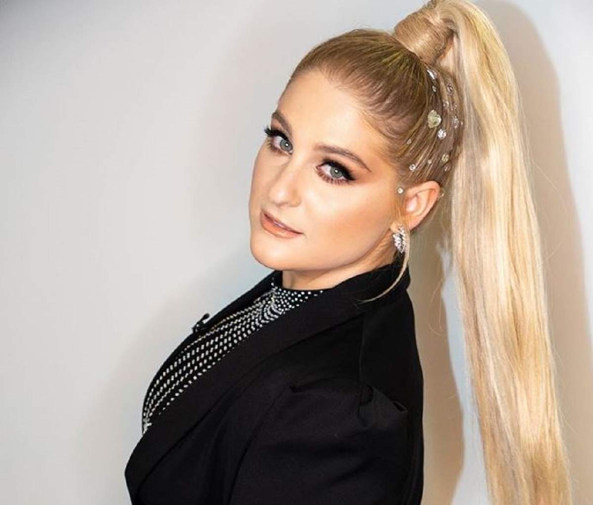 Meghan Trainor poarta o haina neagra, are parul prins si stelute in cap