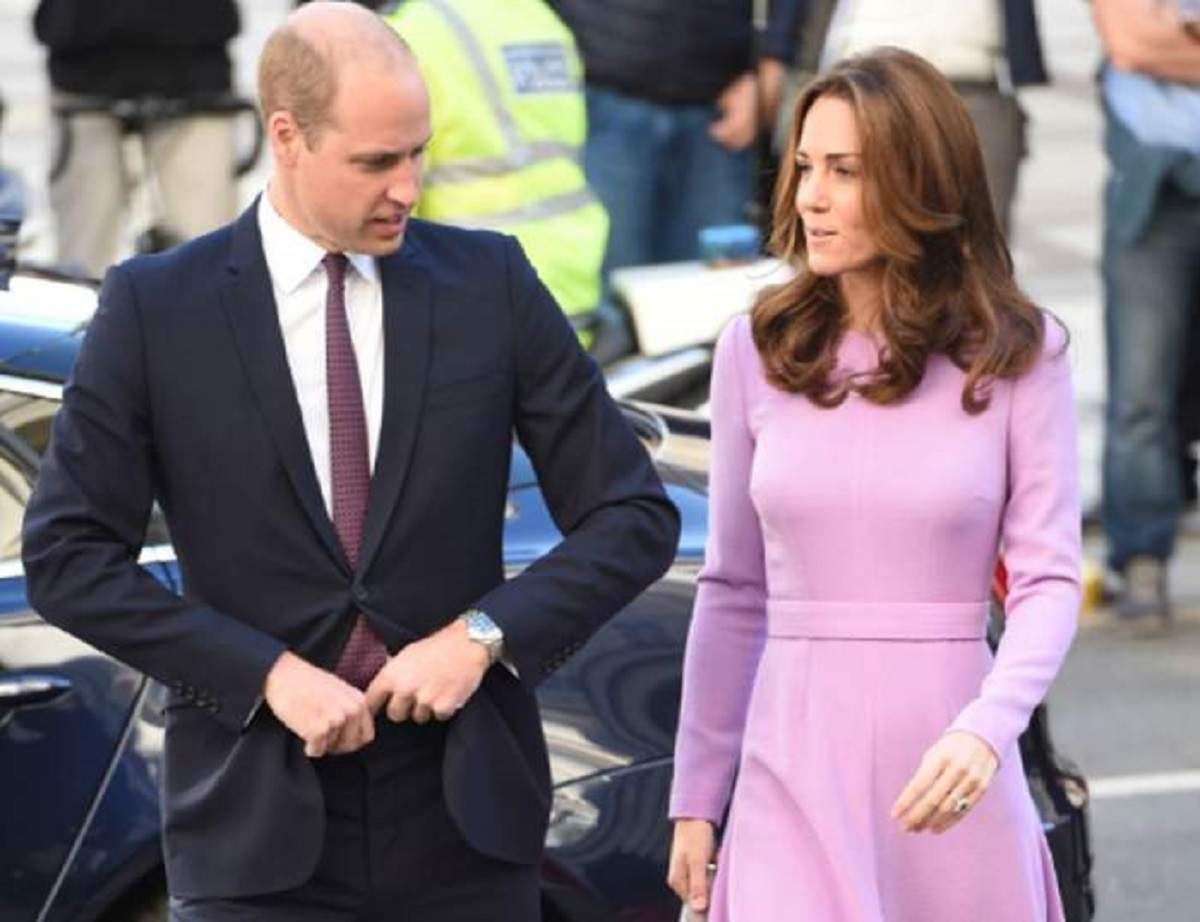 Prinţul William şi Kate Middleton merg pe stradă. El poartă in costum negru, iar ea o rochie roz.