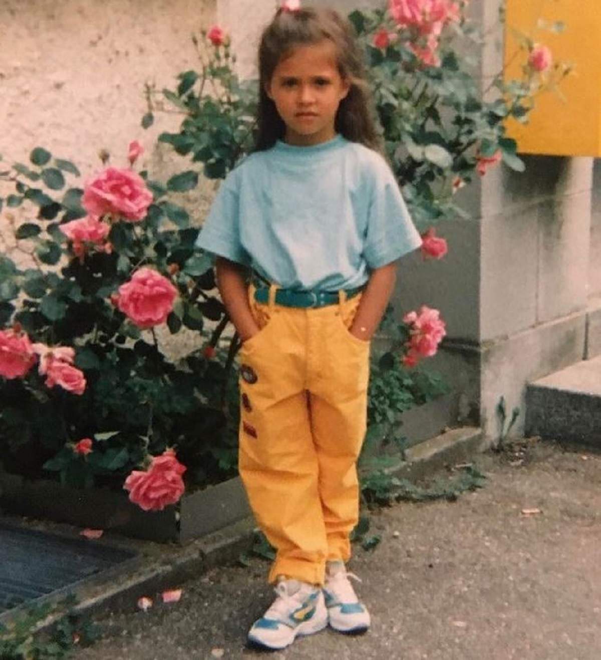 Antonia într-o poză realizată în copilărie. Artista purta un tricou bleu și pantaloni oranj. În spatele ei este o tufă de trandafiri roz.