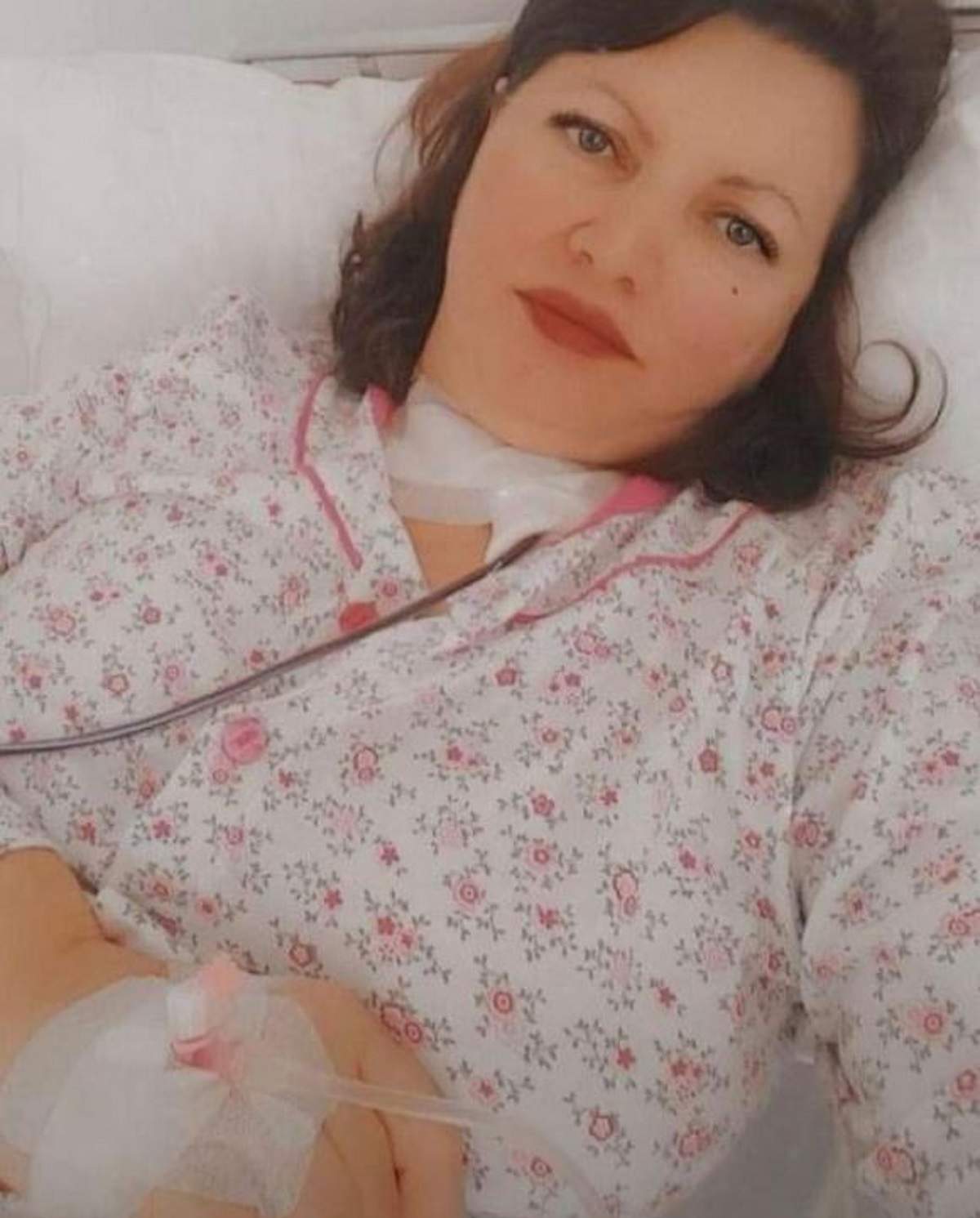 Gina Matache se află pe patul de spital. Mama Deliei este pe perfuzii și poartă o pijama albă.