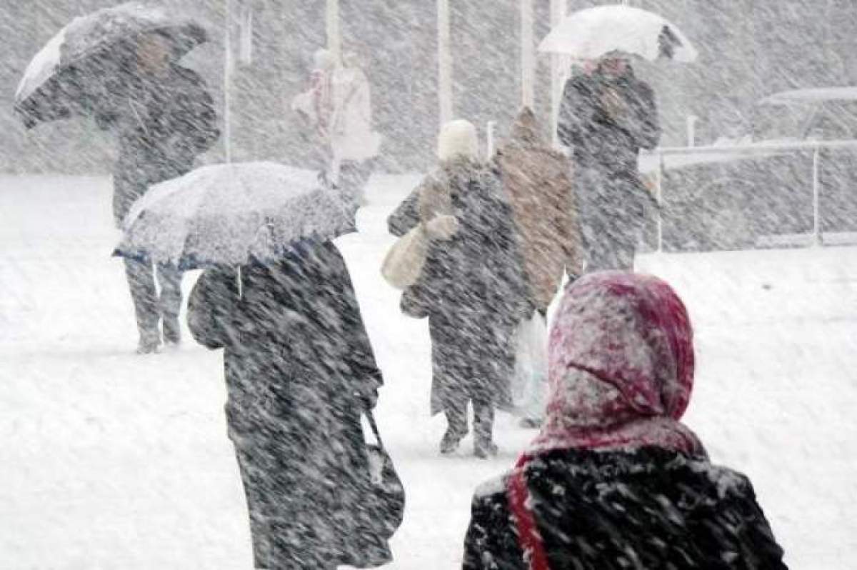 Oameni cu umbrele pe viscol de zăpadă