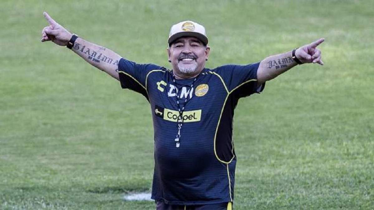 O imagine cu Maradona de când era în viață. Fotbalistul se afla pe teren și era îmbrăcat în echipament sportiv. Acesta zâmbea larg și avea mâinile întinse în aer, pe orizontală.