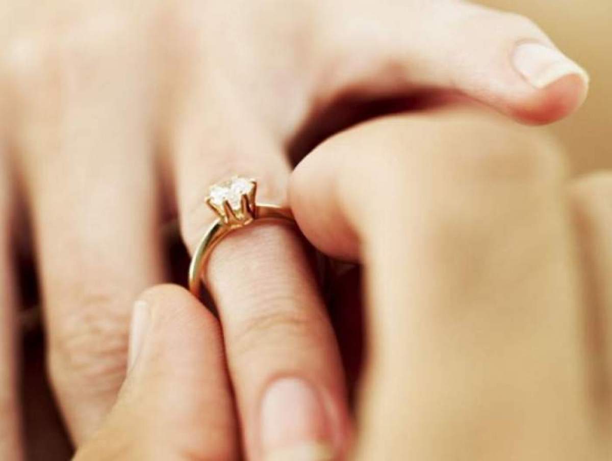 Imagine cu un mana unui barbat care ii aseaza inelul de logodna pe degetul unei femei