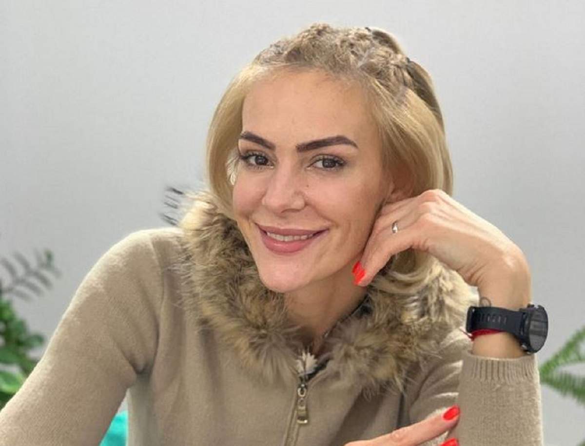 Roxana Ciuhulescu e îmbrăcată cu un pulover crem închis. Blondina zâmbește larg și are o mână la nivelul bărbiei. Vedeta poartă un ceas negru.