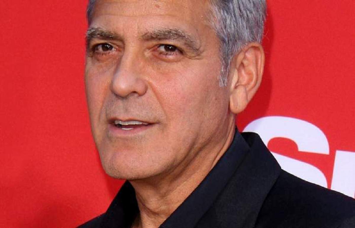George Clooney se află la un eveniment. Actorul este îmbrăcat cu un costum negru și are gura întredeschisă.