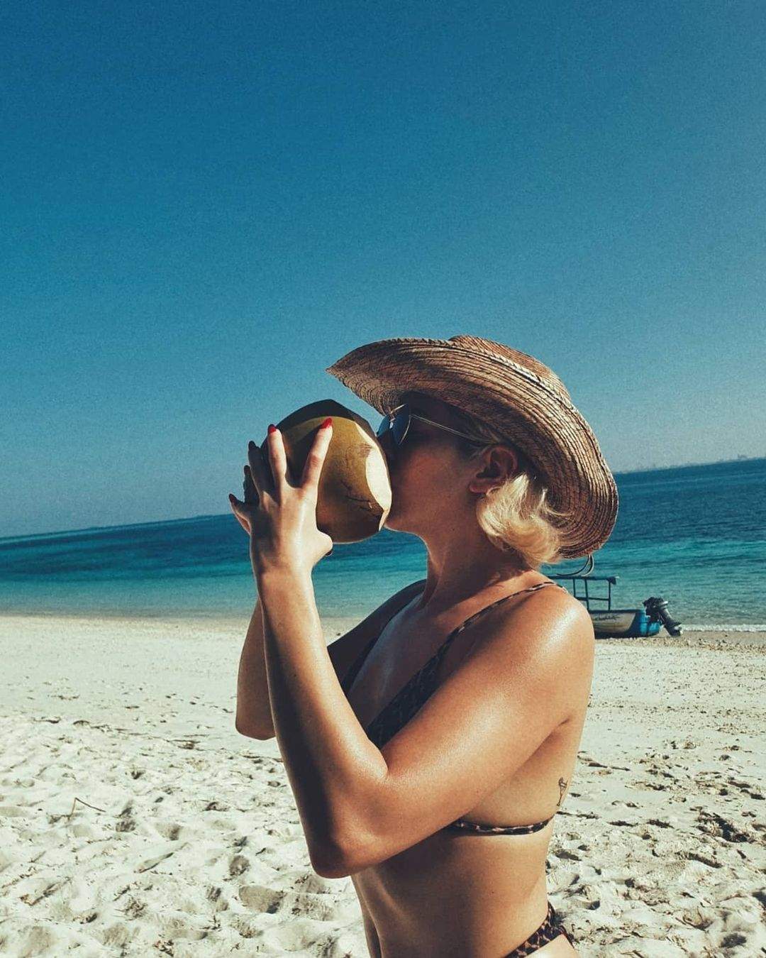 Lidia Buble este pe plaja in costum de baie, bea dintr-o nuca de cocos