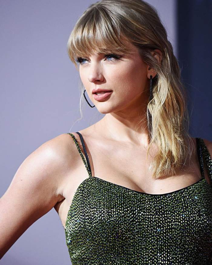 Taylor Swift este la o gala, poarta o rochie verde inchis cu bretele si are parul prins in laterale