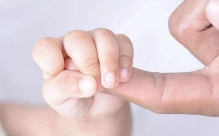 Un bebeluș îi apucă cu mâna degetul unui adult.