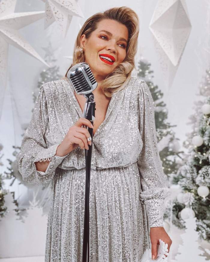 Gina Pistol poarta o rochie argintie, are parul aranjat si canta
