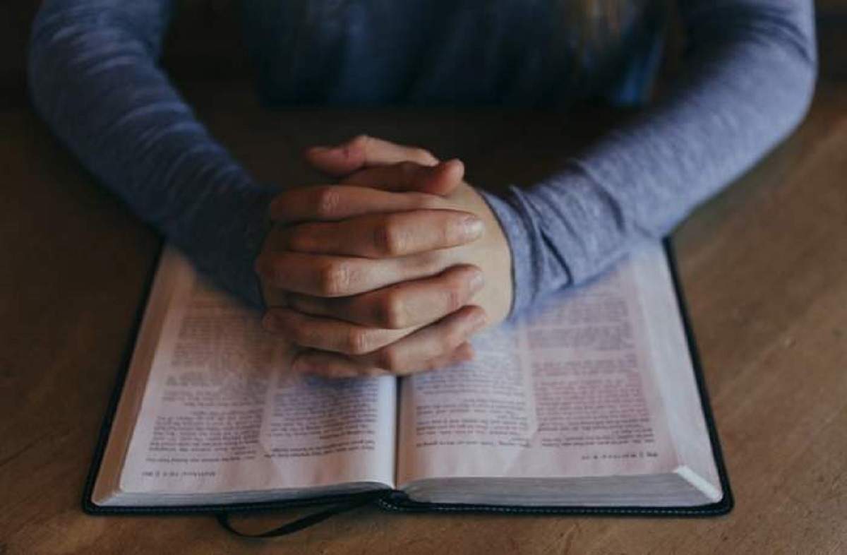 O carte de rugăciuni deschisă. Deasupra ei sunt așezate doi mâini împreunate.