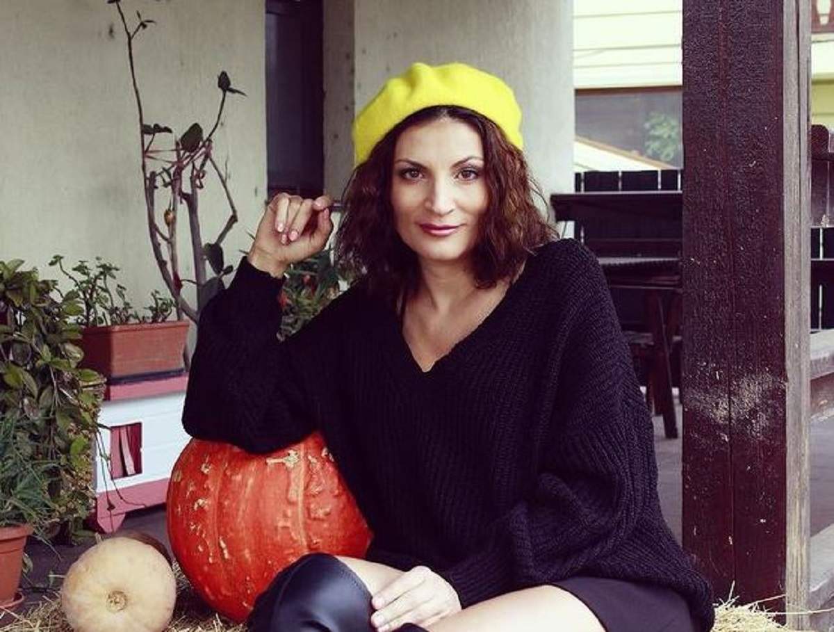Ioana Ginghină stă pe scări, în fața casei. Artista poartă o rochie neagră și beretă galbenă.
