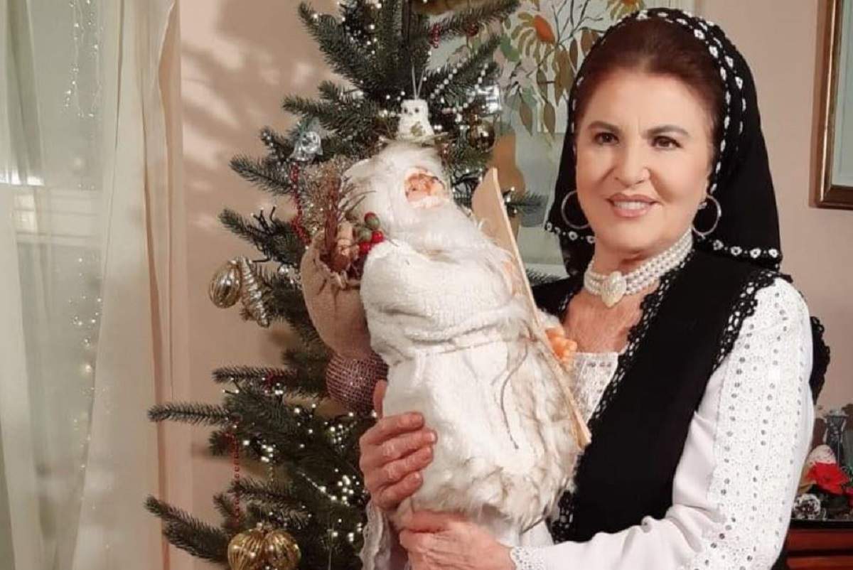Irina Loghin e îmbrăcată în port popular. Artista ține în mână o jucărie cu Moș Crăciun.