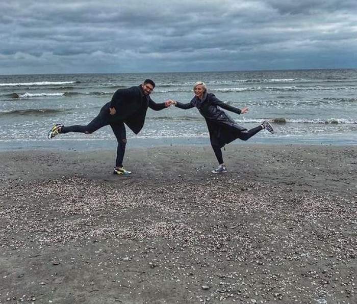Ionuț Gojman și iubita lui se află la mare. Cei doi sunt îmbrăcați în negru și au un picior ridicat în aer.