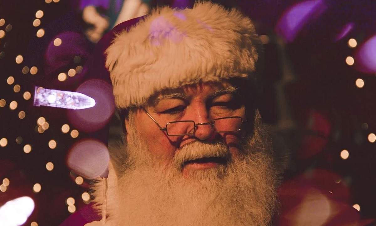 O imagine cu un om costumat în Moș Crăciun. Acesta privește în jos.