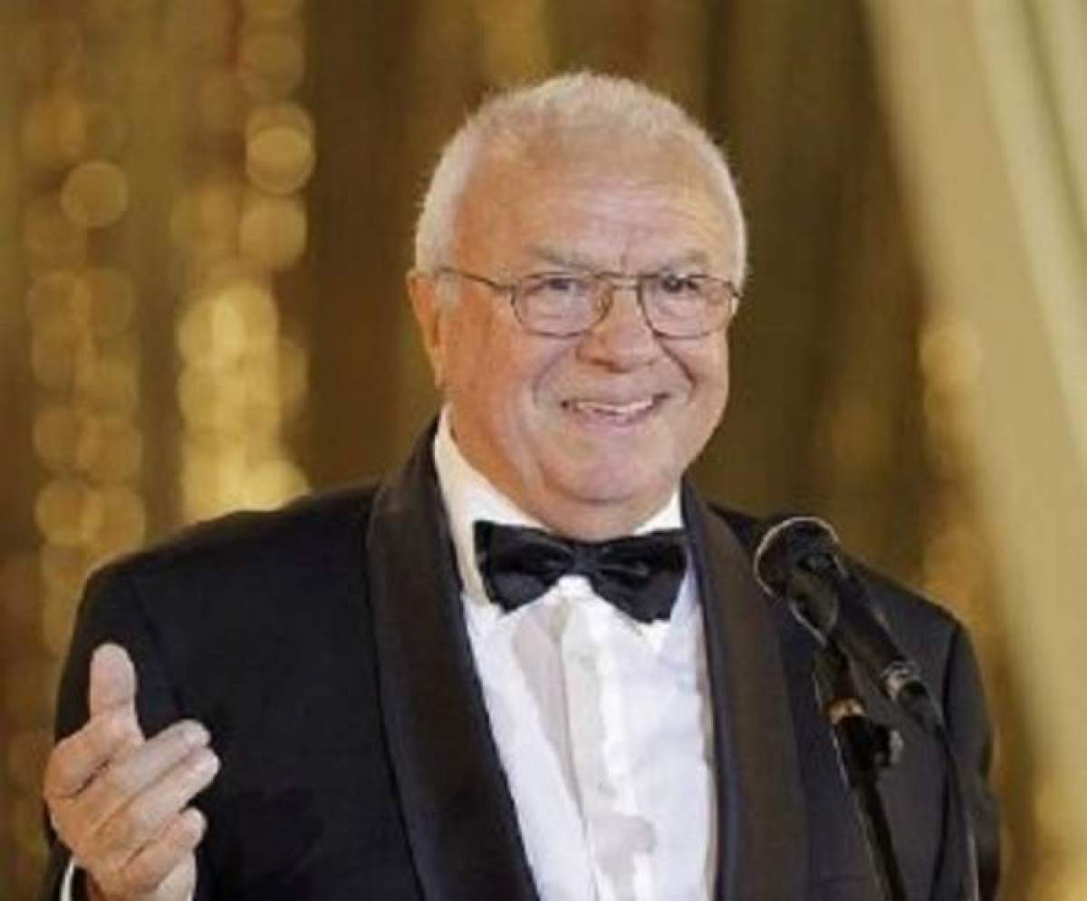 Alexandru Arsinel este la o gala, vorbeste la pupitru, zambeste si poarta costum negru cu papion