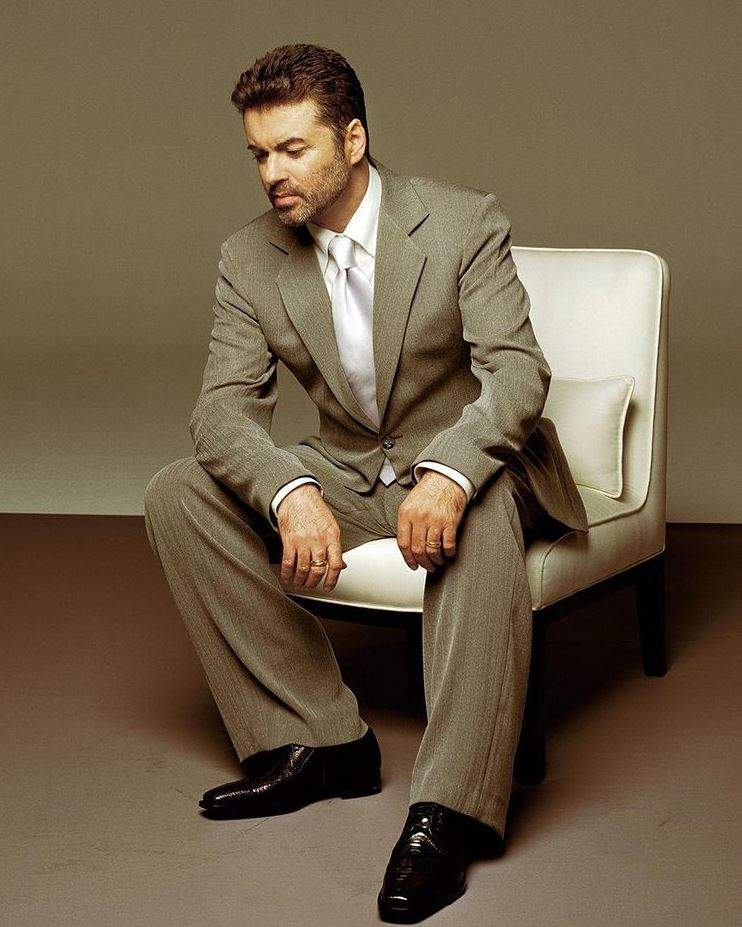 George Michael, îmbrăcat în costum, stând pe un fotoliu