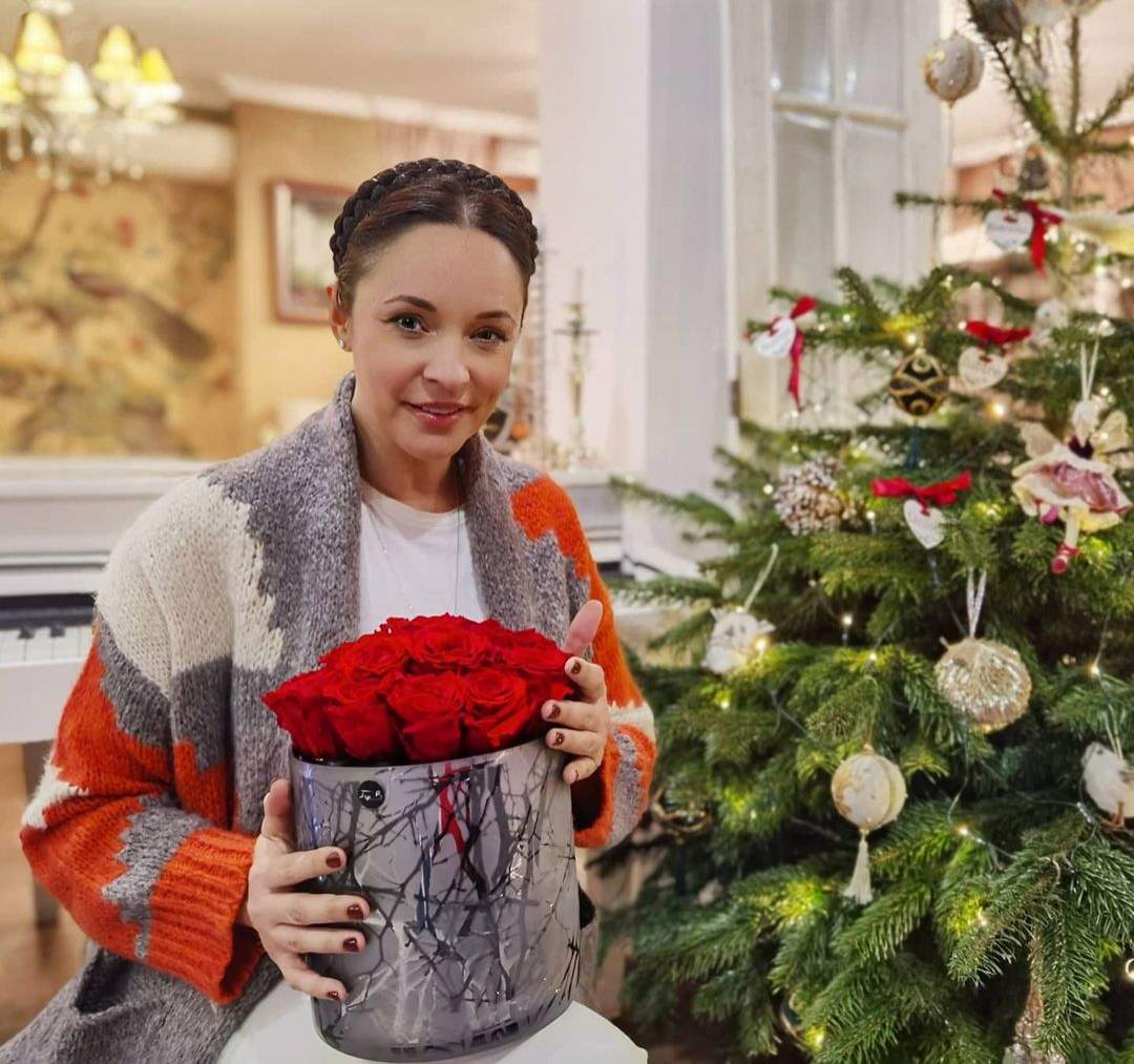 Andreea Marin cu un buchet mare de trandafiri roșii, lângă brad.