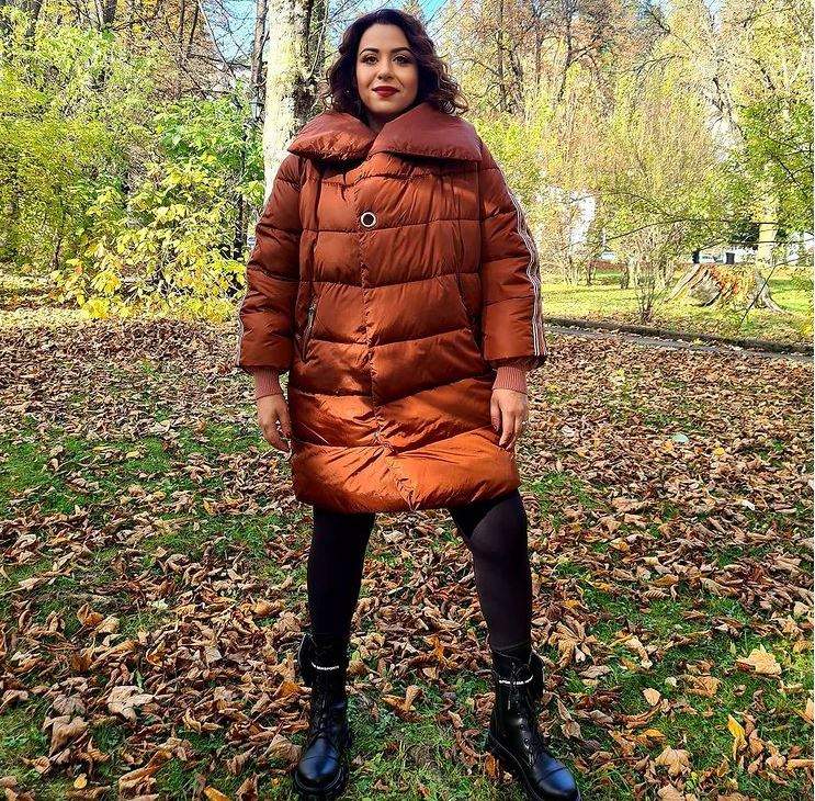 Oana Roman se află în parc. Vedeta poartă o geacă oversized, maro, și pantaloni negri, mulați.