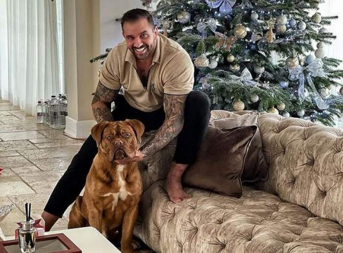 Alex Bodi stă pe canapea. Afaceristul se joacă cu câinele său. În spatele lor se vede bradul de Crăciun,