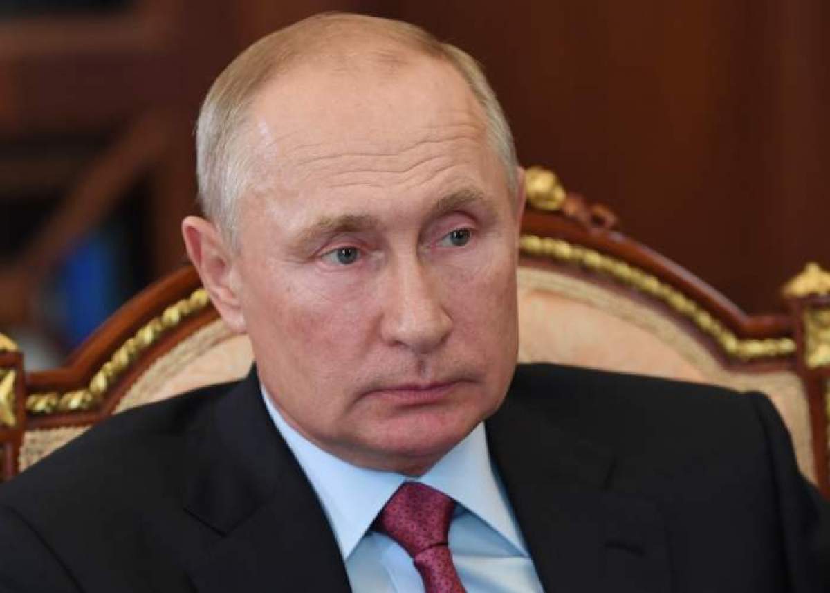 Vladimir Putin sta pe un scaun, poarta costum cu cravata rosie