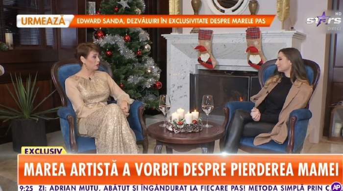 Adriana Antoni stă pe un fotoliu albastru. Artista e îmbrăcată într-o rochie crem și dă un interviu pentru Antena Stars. Artista vorbește despre mama ei.