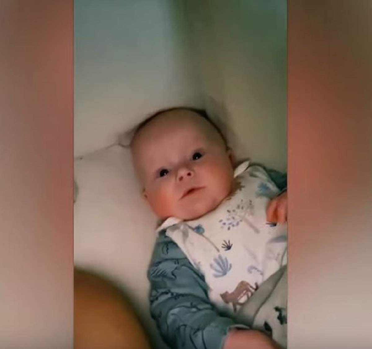 Bebelușul Reuben stă întins pe spate, în pat. Micuțul din Marea Britanie poartă o bluză bleu cu alb.