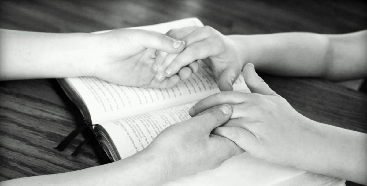 Două persoane se țin de mâini deasupra unei cărți religioase pentru a se ruga