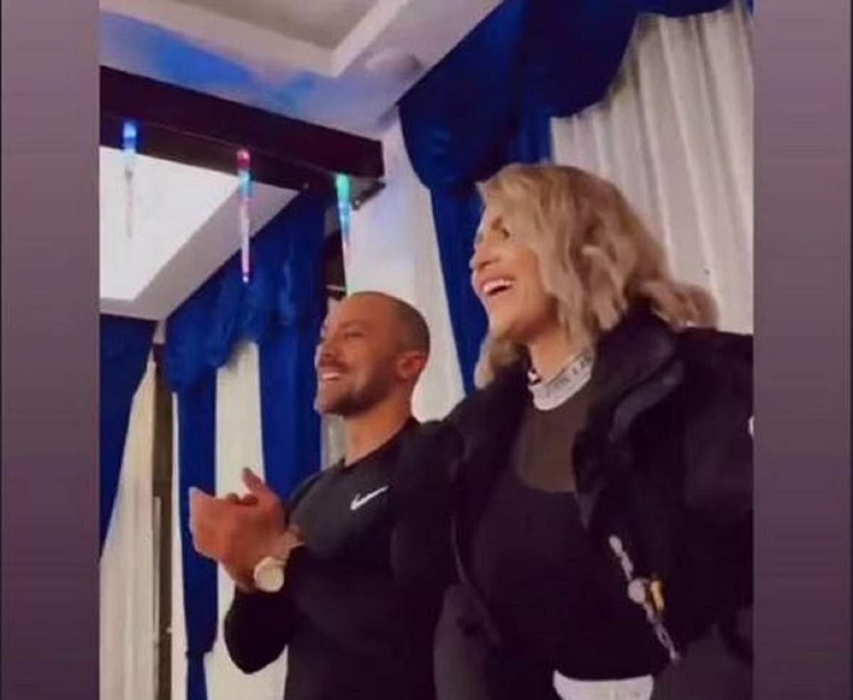 Oana Radu și soțul ei, Cătălin Dobrescu, se află într-un restaurant. Cei doi sunt îmbrăcați în negru. El aplaudă, iar ea zâmbește larg.