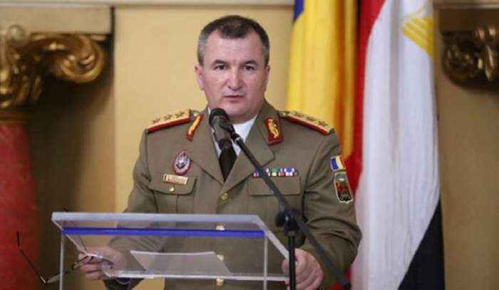 Nicolae Ciucă, premierul interimar al țării, poartă o uniformă verzuie. Acesta ține un discurs la microfon.