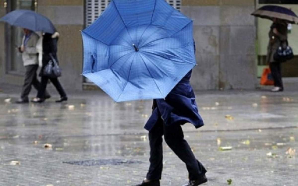 O femeie in plină stradă care se află sub umbrelă în mijlocul unei furtuni