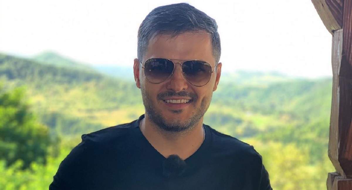 Liviu Vârciu cu ochelari de soare, îmbrăcat cu un tricou negru, pozează în fața unor dealuri verzi