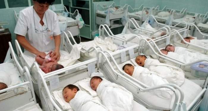 Bebeluși la maternitate lângă care stă o asistentă