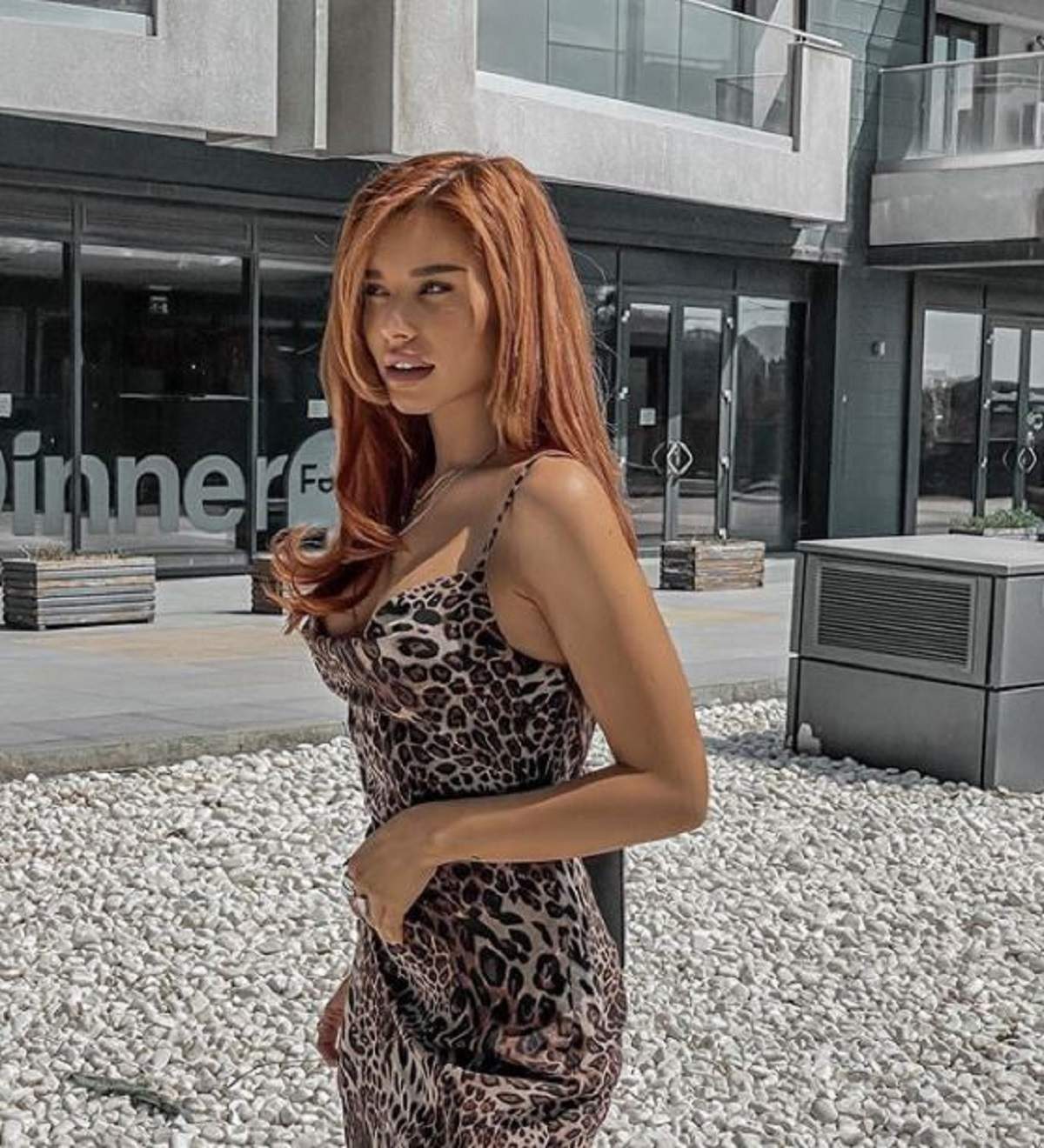 Carmen Grebenișan zâmbește în fața unui magazin și se uită în față, în timp ce poartă o rochie scurtă cu imprimeu de leopard