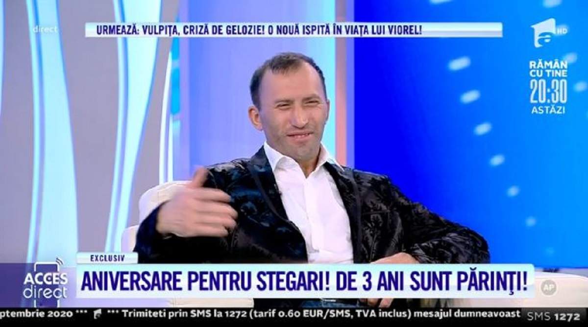 Viorel este așezat pe scaun, în platoul „Acces Direct”. Bărbatul este îmbrăcat în costum negru și cămașă albă și zâmbește.